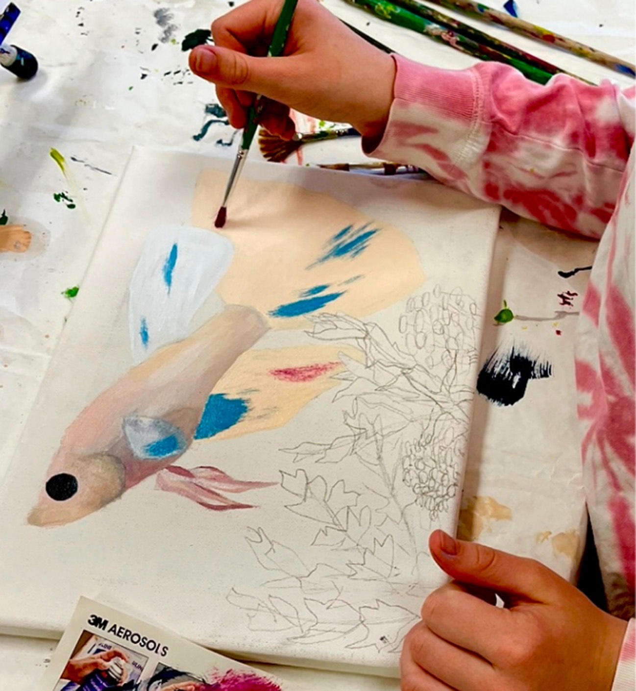 person working on painting in progress. the painting depicts a fish among aquatic plants