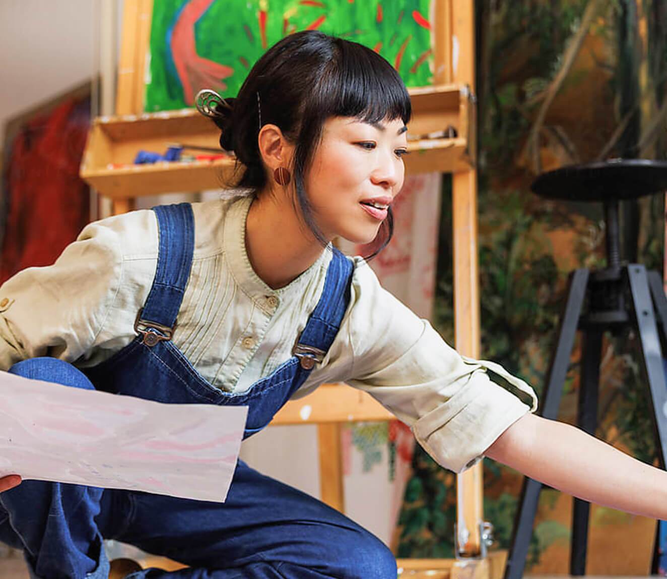 young woman kneeling while holding an artwork in progress