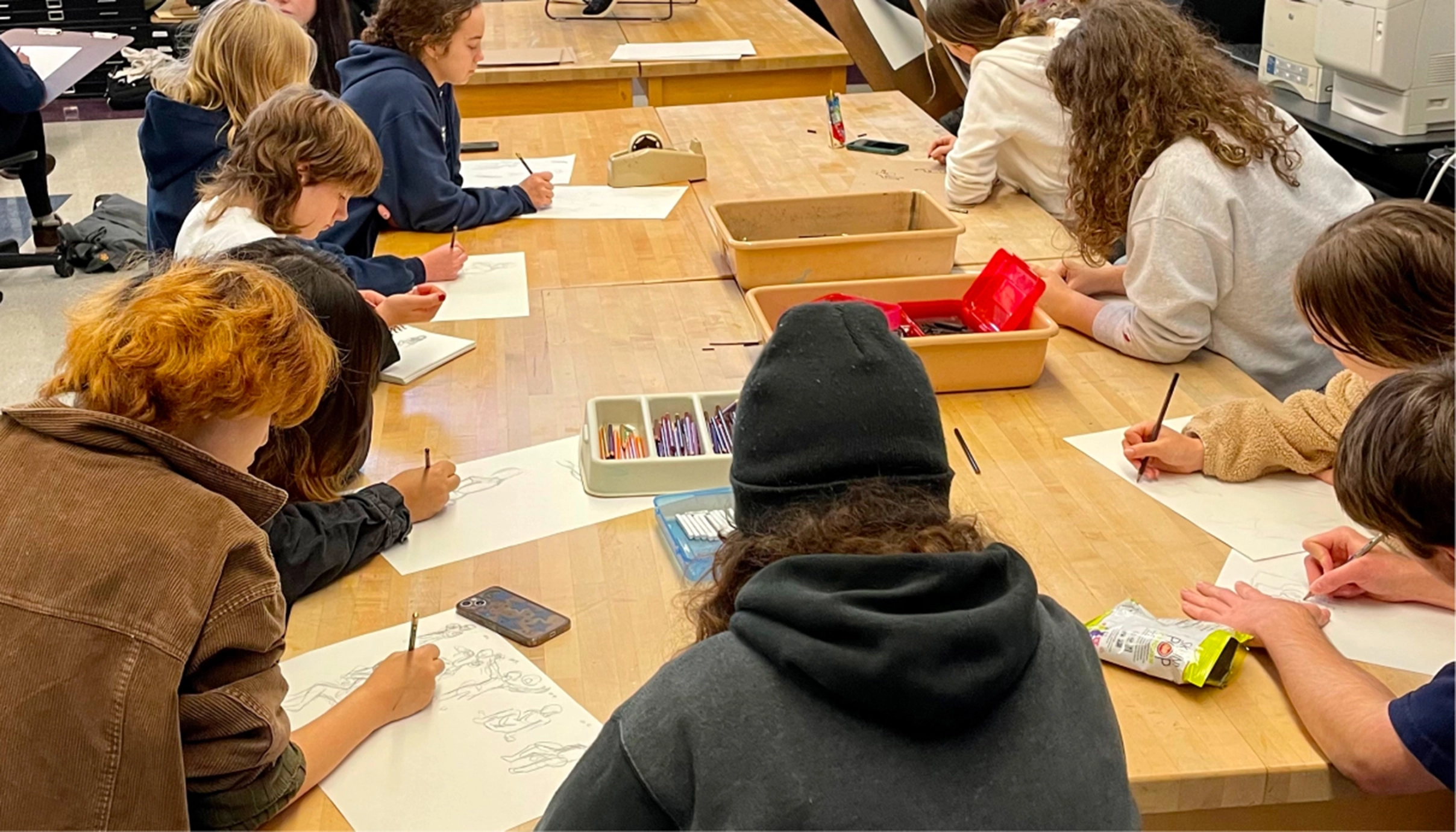 students seated at long tables and working on drawings