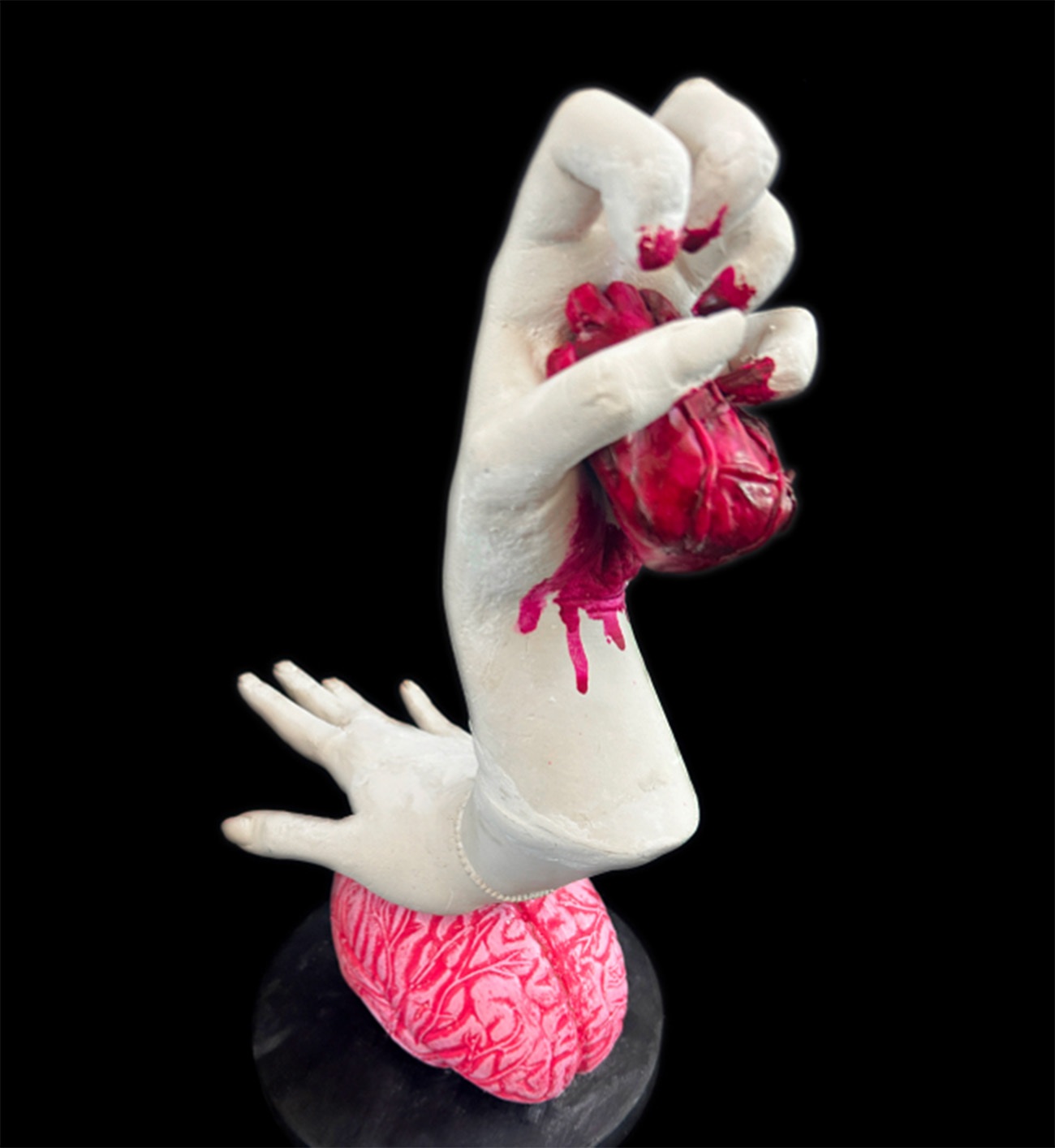 Sculpture of two hands attached both ends of the same arm and posed vertically. The top hand holds a heart. The bottom hand rests on top of a brain.