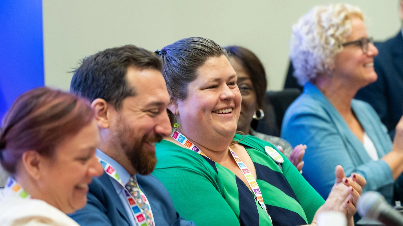 Group photo of people sitting in a row. They are smiling and clapping for a speaker